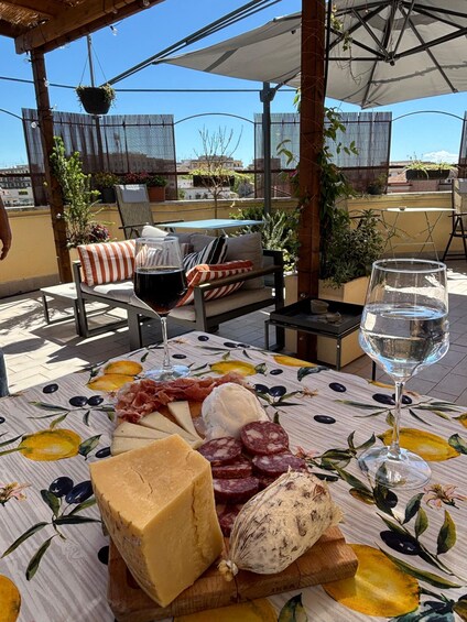 A table with a cheese platter, wine, and a glass of water on a patio with a view of the city. 4