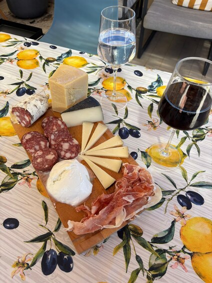 A charcuterie board with various cheeses, cured meats, and a glass of red wine on a table with a floral tablecloth. 2