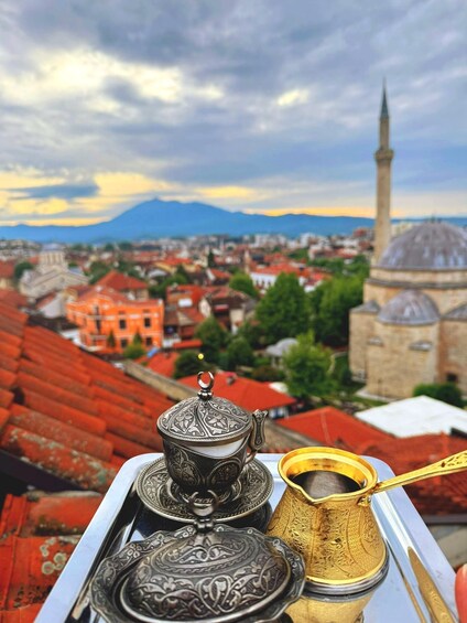 A tray with a teapot and a brass coffee pot, a mosque with a minaret, and a cityscape with red-roofed buildings. 3
