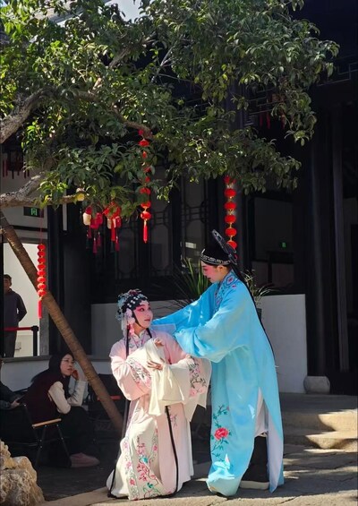 A person in traditional attire performing a dance under a tree adorned with red lanterns. 1