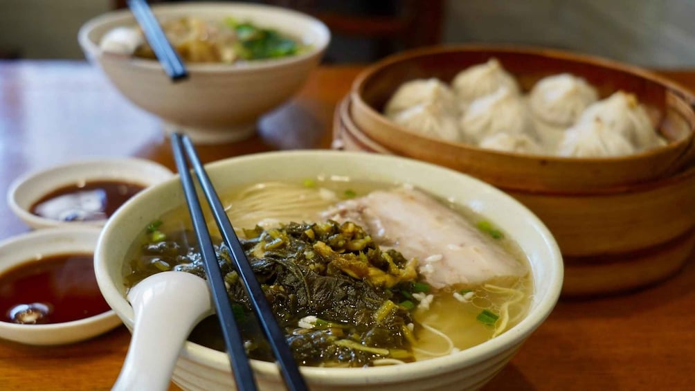 A bowl of soup with chopsticks, a bowl of dumplings, and a small dish of sauce. 1