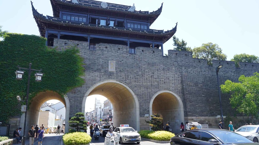 A traditional Chinese gate with three arches, a pagoda, and a busy street with pedestrians and vehicles. 5