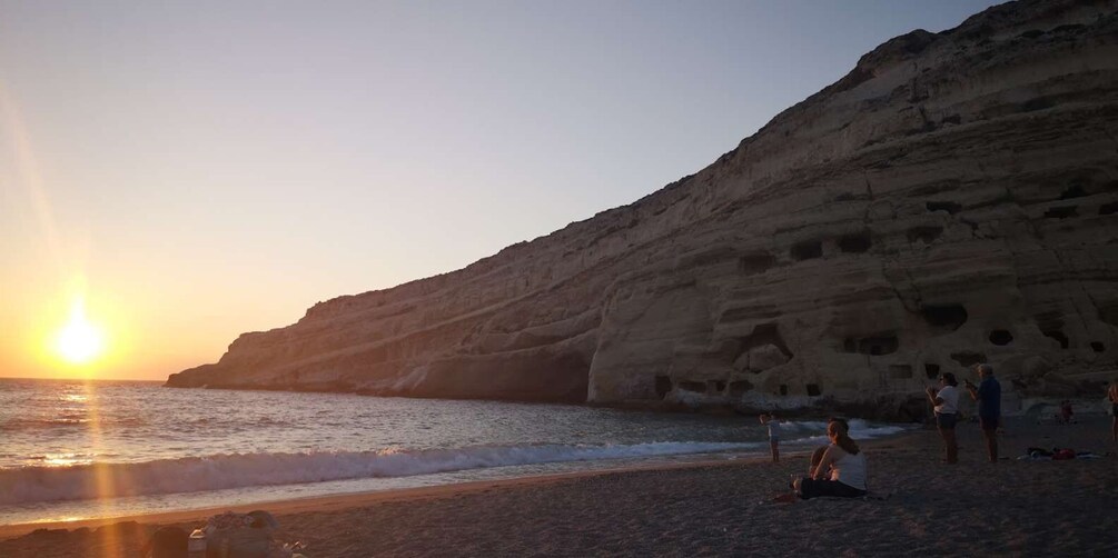 A sunset over a rocky coastline with people on the beach. 1