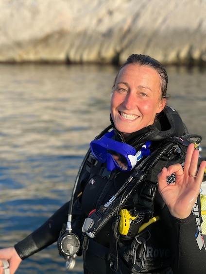 A person in a black wetsuit with a blue scarf, holding a yellow device, and standing by a body of water. 1