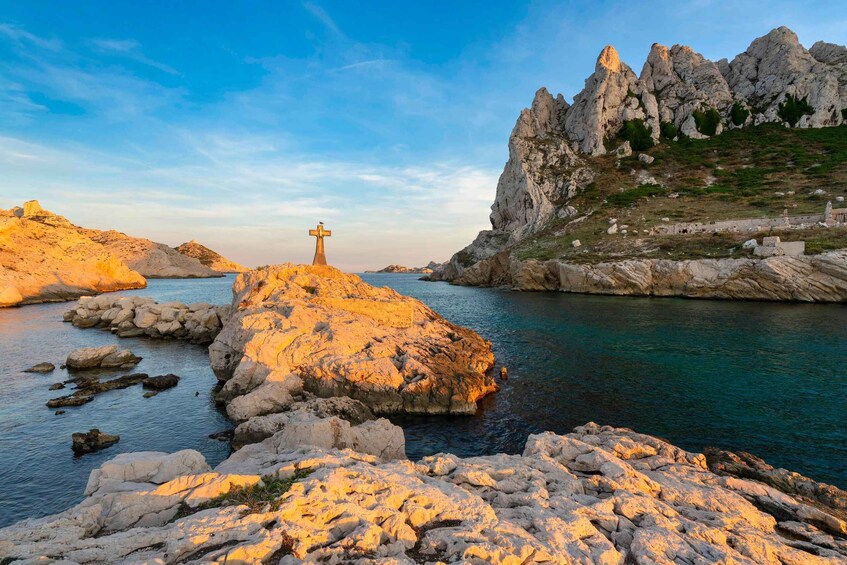 A rocky coastline with a cross on a rock, clear blue water, and rugged cliffs. 4