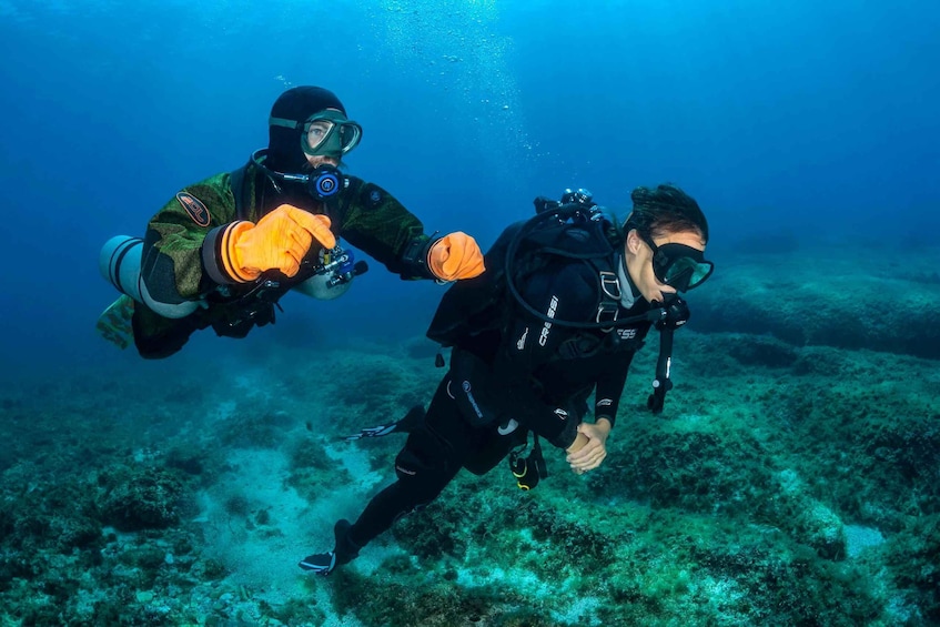 Two scuba divers underwater with scuba gear, one wearing a camouflage wetsuit and the other in black. 2