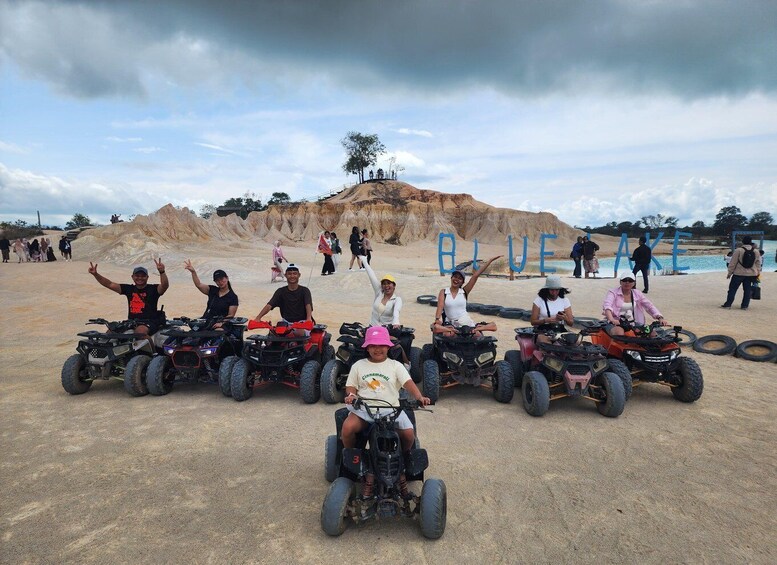 A group of people on ATVs at a sandy area with a large pile of earth in the background and the word 'BLUE' spelled out in the distance. 5