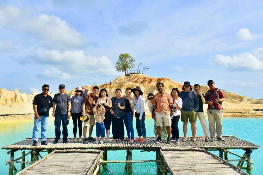 A group of people standing on a wooden pier with a desert landscape and clear blue water in the background. 2