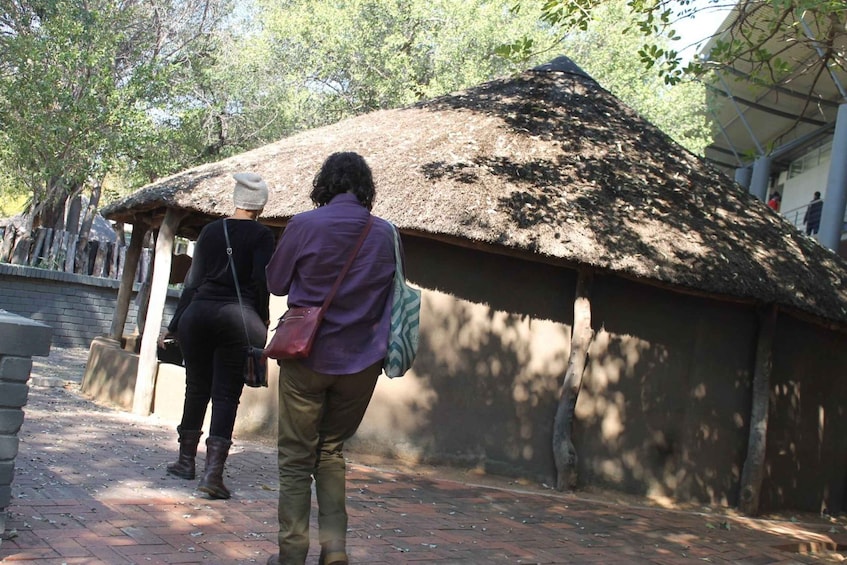 A rustic hut with a thatched roof, a brick pathway, and trees in the background. 1