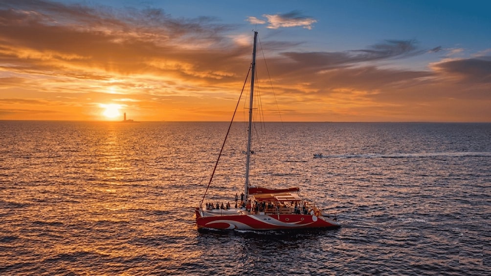 A sailboat with passengers at sunset on the ocean. 1