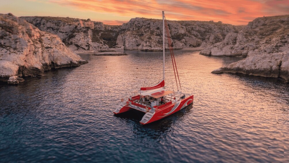 A red and white sailboat on calm waters surrounded by rocky cliffs. 4
