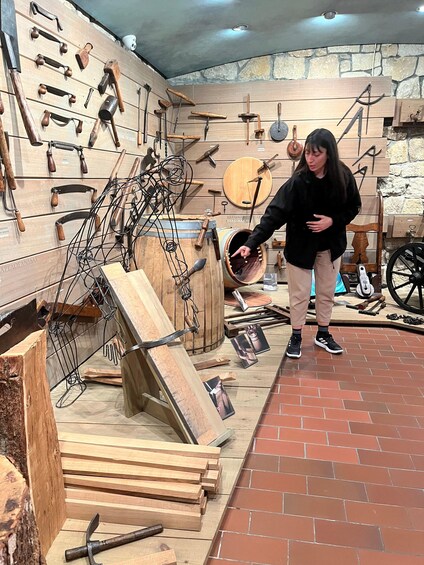 A person examining a wooden barrel in a museum with various tools and historical items displayed on the walls. 4