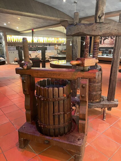 An antique distillation apparatus with wooden barrels and metal components, displayed indoors with tiled flooring. 5