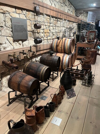 Antique barrels, metal containers, and wooden vats on display against a stone wall. 3