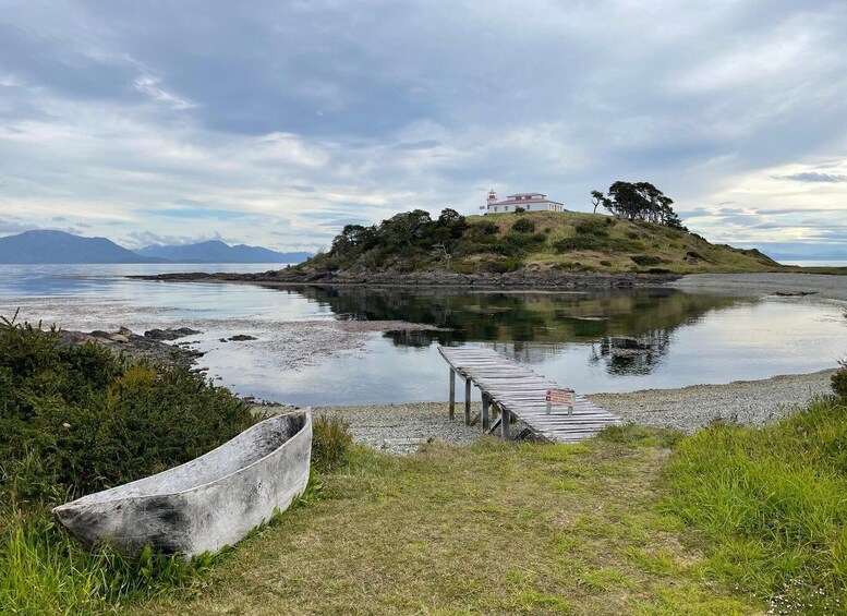 A coastal landscape with a lighthouse on a small island, calm water, and a wooden dock. 2