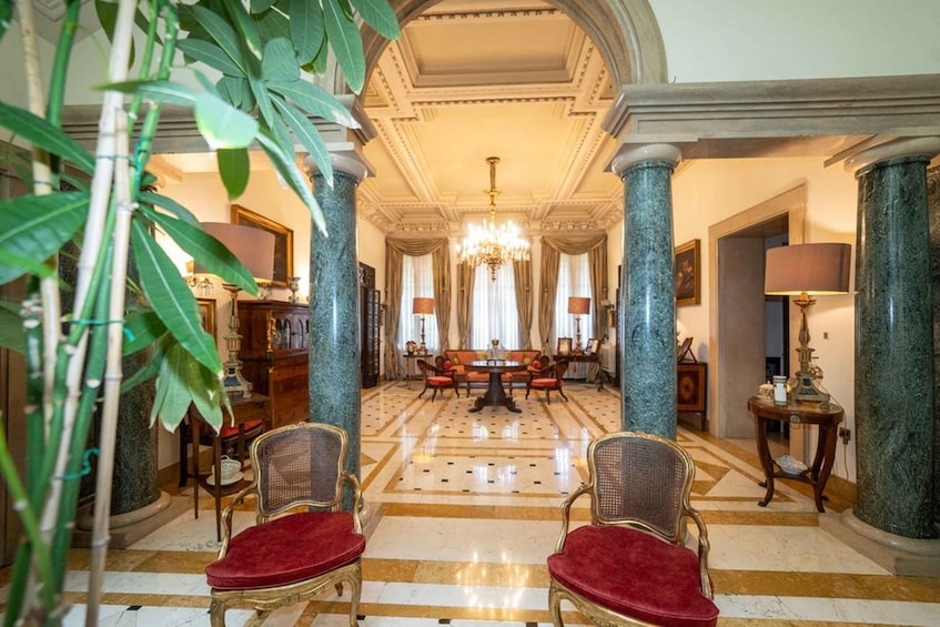 Un salón majestuoso con columnas de mármol, un candelabro y una mesa redonda con sillas. 2