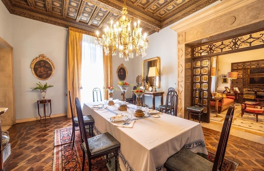 Un comedor formal con una larga mesa dispuesta para una comida, techo ornamentado y decoración tradicional. 1