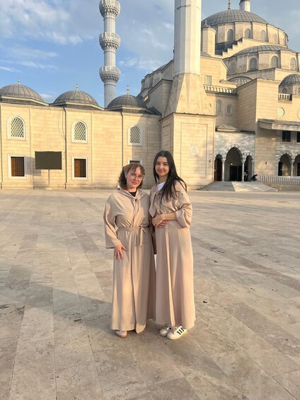 Two people standing in front of a large mosque with domes and minarets. 2
