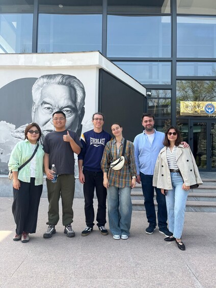 A group of people standing in front of a building with a large mural and a glass door with a logo. 4