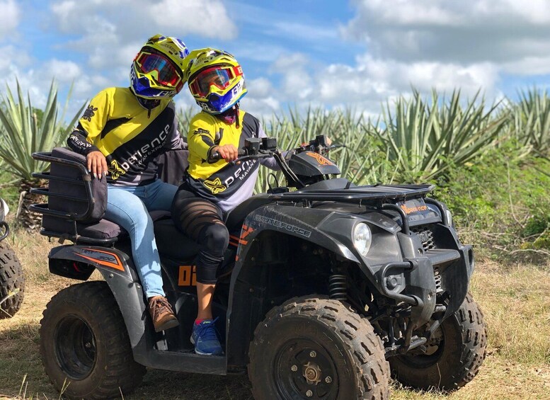 Two people on an ATV in a field with agave plants. 2