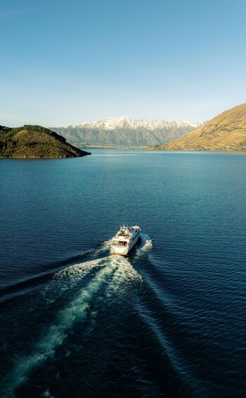 A boat moving across a calm lake with mountains in the background. 2