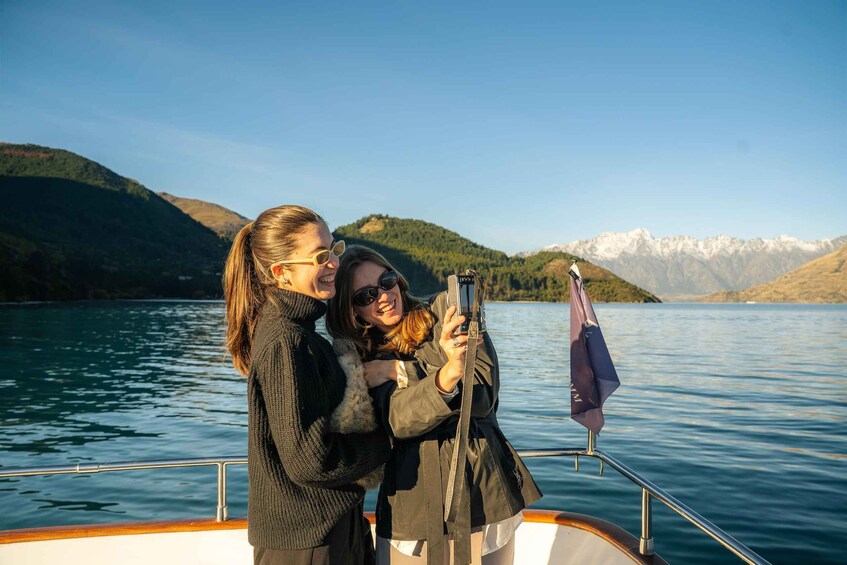 Two people on a boat taking a selfie with a lake and mountains in the background. 5