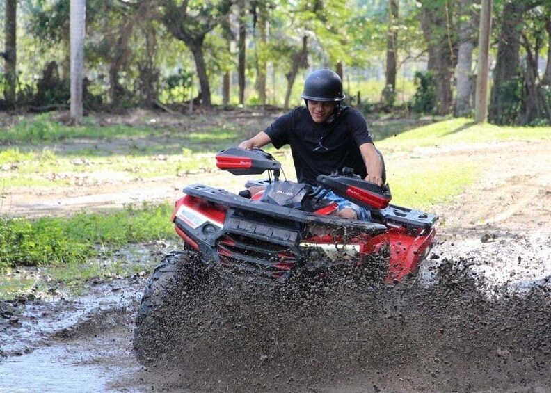 A person riding a red ATV on a muddy trail surrounded by trees. 2