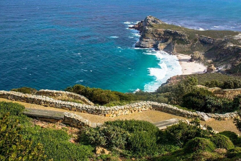 A coastal landscape with a rocky cliff, a beach, and a stone wall. 2