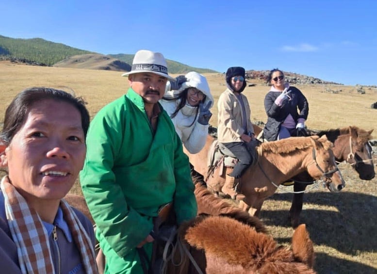 A group of people on horseback in a grassy field with hills in the background. 5