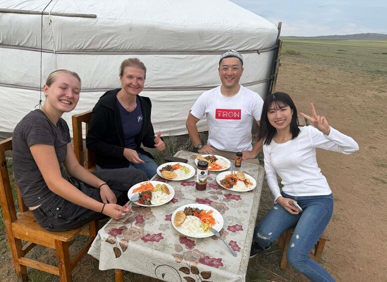 Four people sitting at a table with food in front of a tent in a grassy field. 3