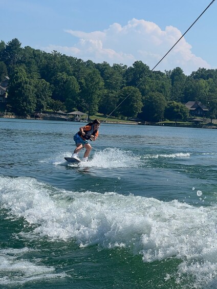 A person wakeboarding on a lake with a house and trees in the background. 3