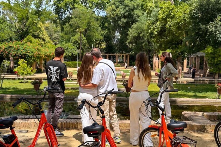 A group of people standing by a pond in a park with bicycles. 2