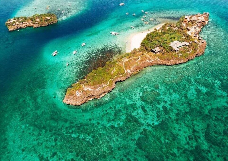 An aerial view of a tropical island with clear turquoise waters, a sandy beach, and scattered boats. 3