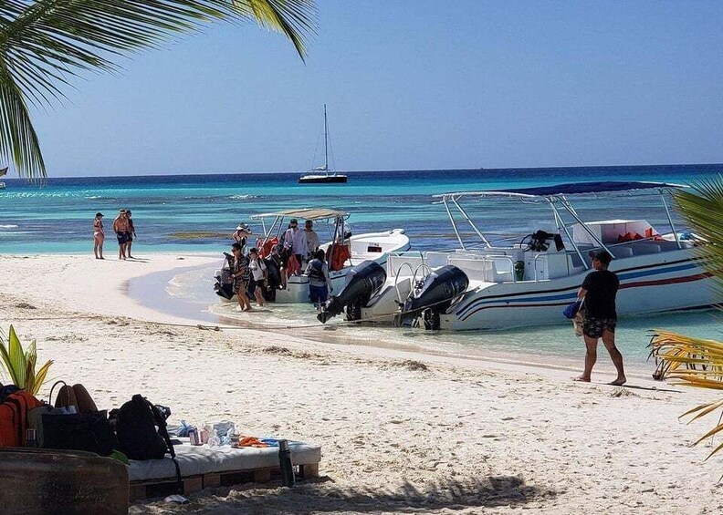 A beach with people, boats, and a sailboat in the water. 2