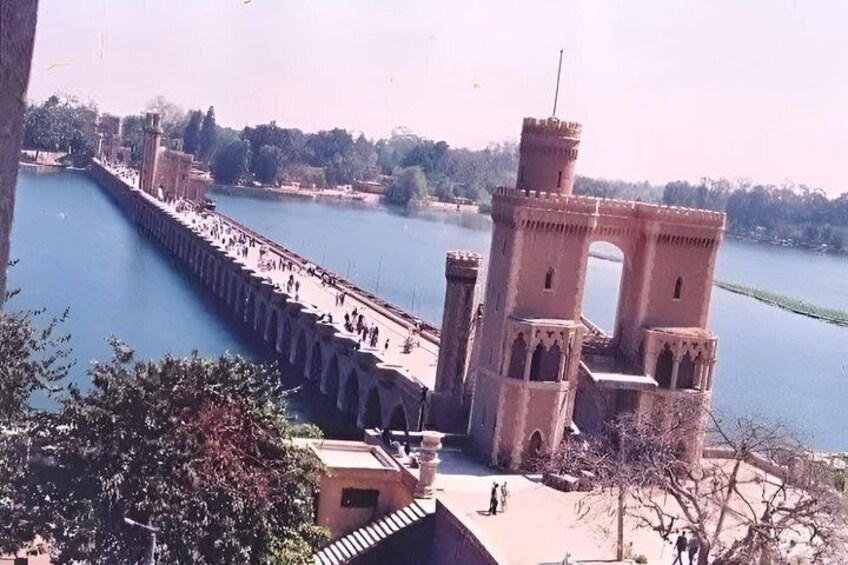 A large stone bridge over water, a tower-like structure, and a tree-lined area. 1