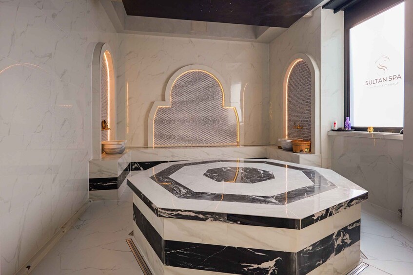 A modern spa interior with a central hexagonal marble platform, arched niches, and a wall-mounted logo. 4