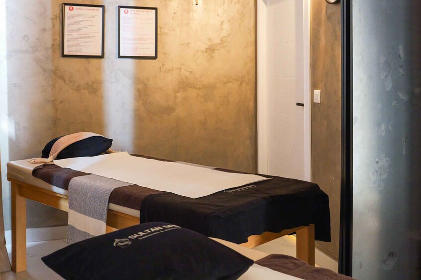 A massage therapy room with two massage tables, a wall with two informational posters, and a door with a frosted glass panel. 2