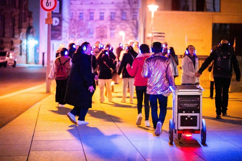 A group of people walking on a city street at night, some wearing headphones. 1