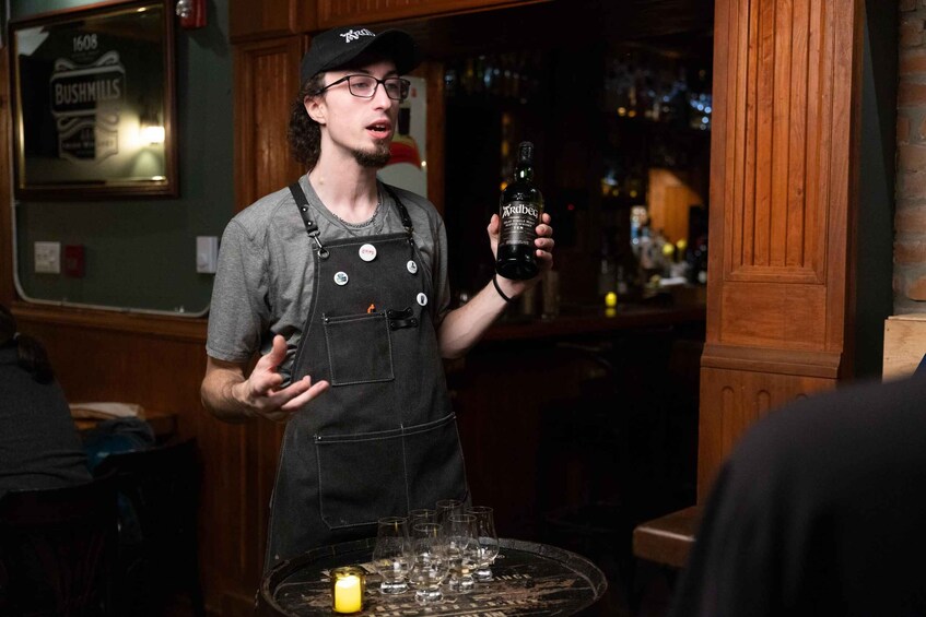 A person in a bar holding a bottle, glasses on a table, and a candle. 2