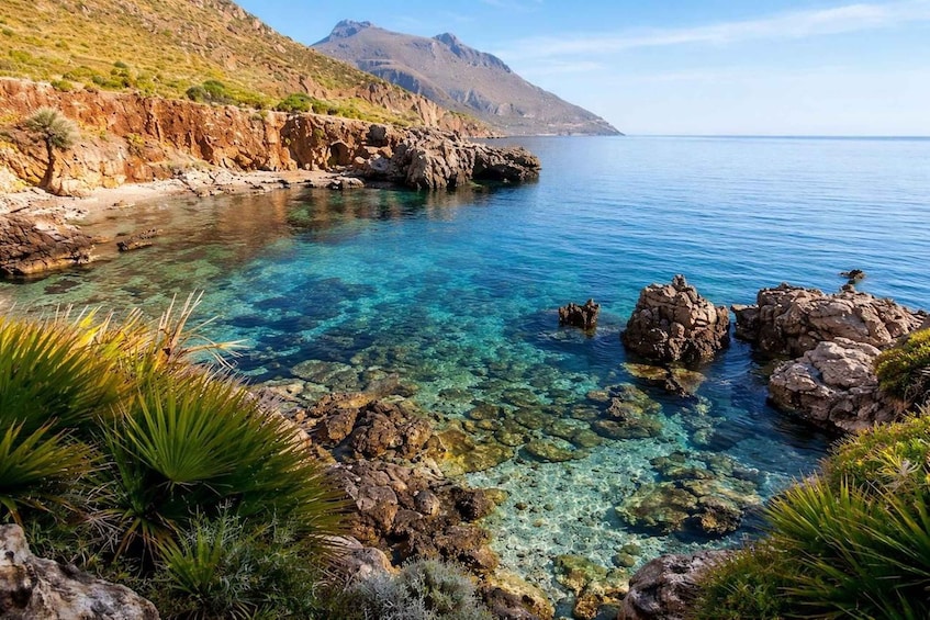 A coastal landscape with clear water, rocky shorelines, and a mountain in the distance. 4