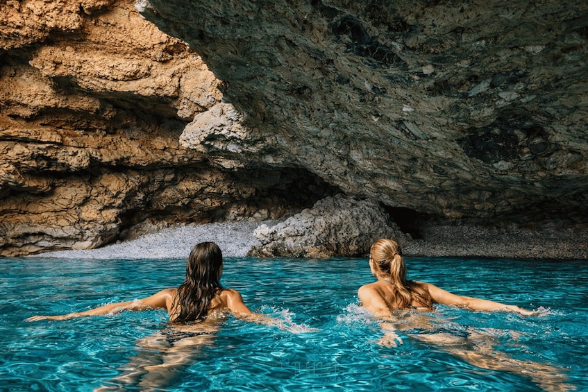 Two people swimming in a pool with a rocky cave in the background. 2