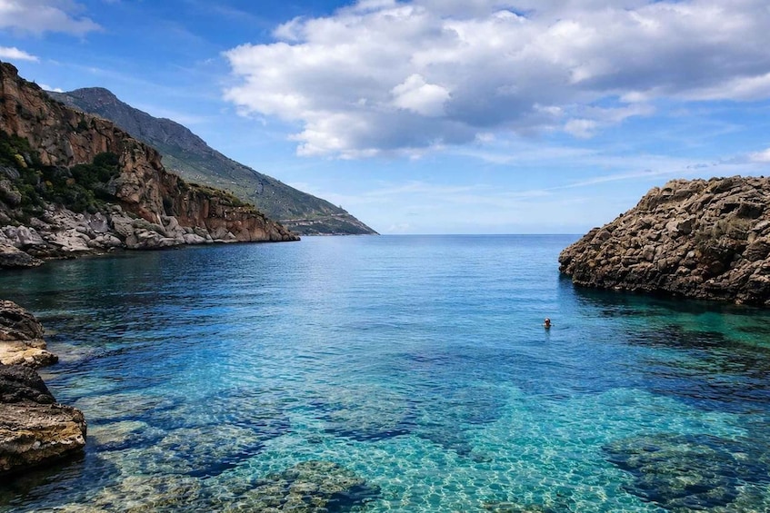 A clear coastal bay with rocky shores and a swimmer in the water. 3