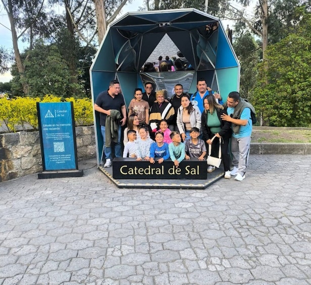 A group of people posing in front of a blue and black structure labeled 'Catedral de Sal' with a QR code and a signboard. 2