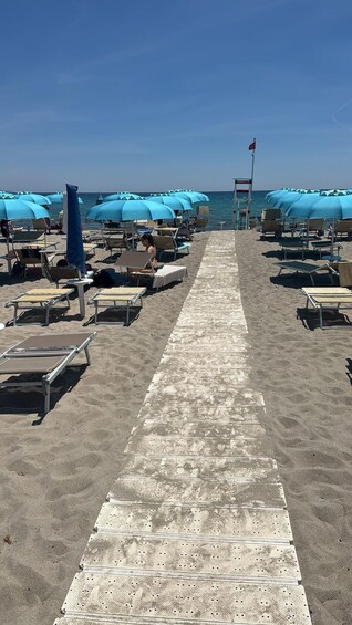 A beach with rows of sun loungers and umbrellas, a lifeguard tower, and a clear blue sky. 3