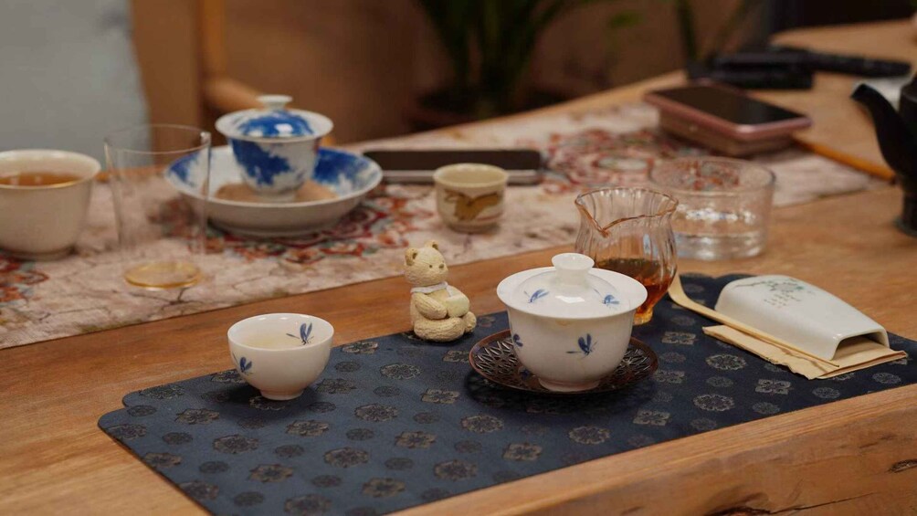 A table with traditional tea ceremony items including cups, a teapot, and a small bear figurine. 1
