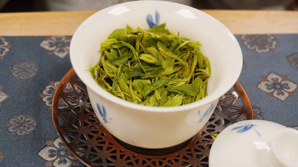 A white teacup with blue floral patterns filled with green tea leaves on a patterned tablecloth. 5