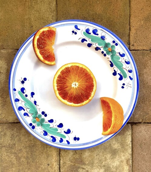 A plate with a floral design and three halves of a blood orange on a tiled floor. 2
