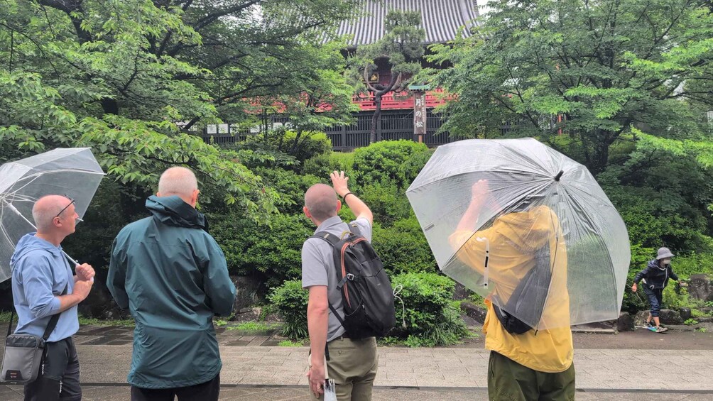 A group of people with umbrellas in a park with trees and a building in the background. 2