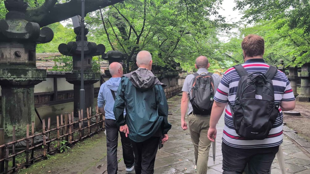A group of people walking along a stone pathway in a wooded area with traditional stone structures. 1