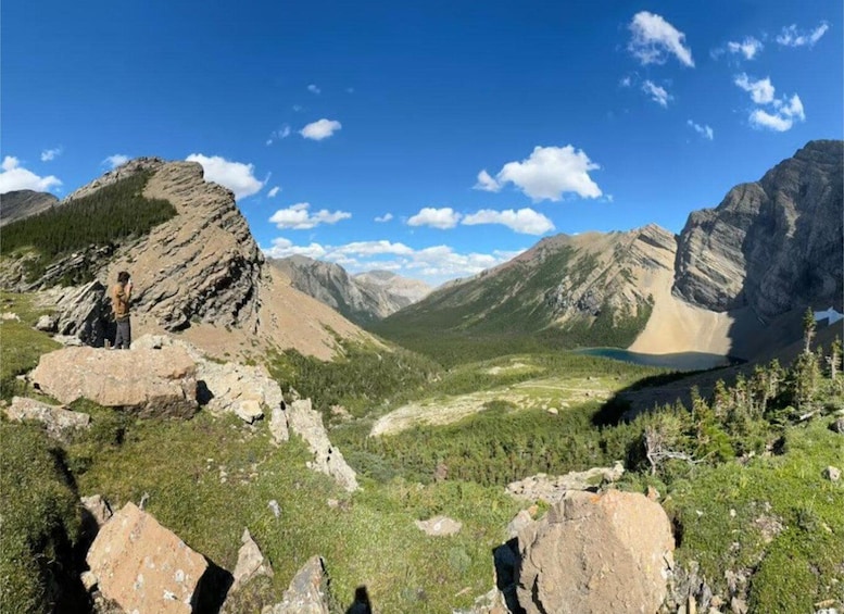 A mountainous landscape with a person standing on a rock, a valley, and a lake. 3